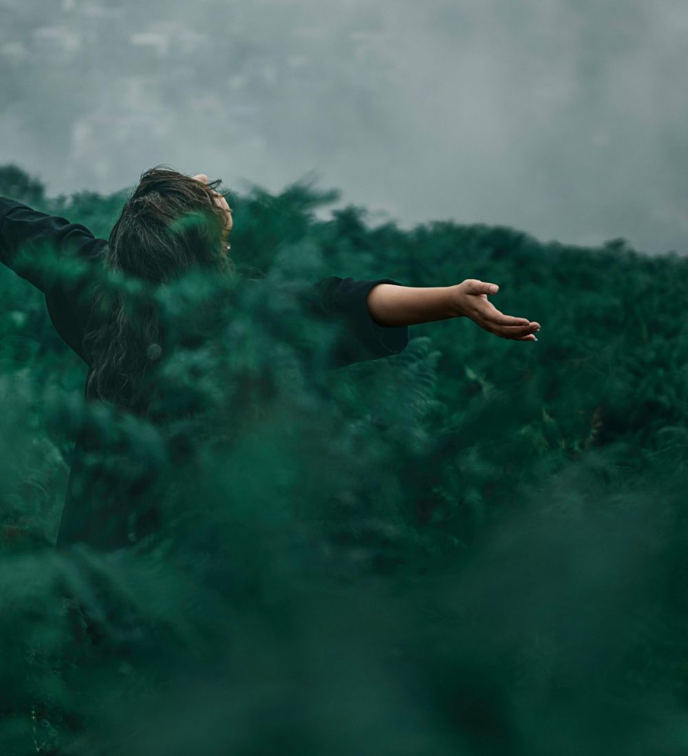 A woman with open arms enjoying freedom in a foggy green landscape.